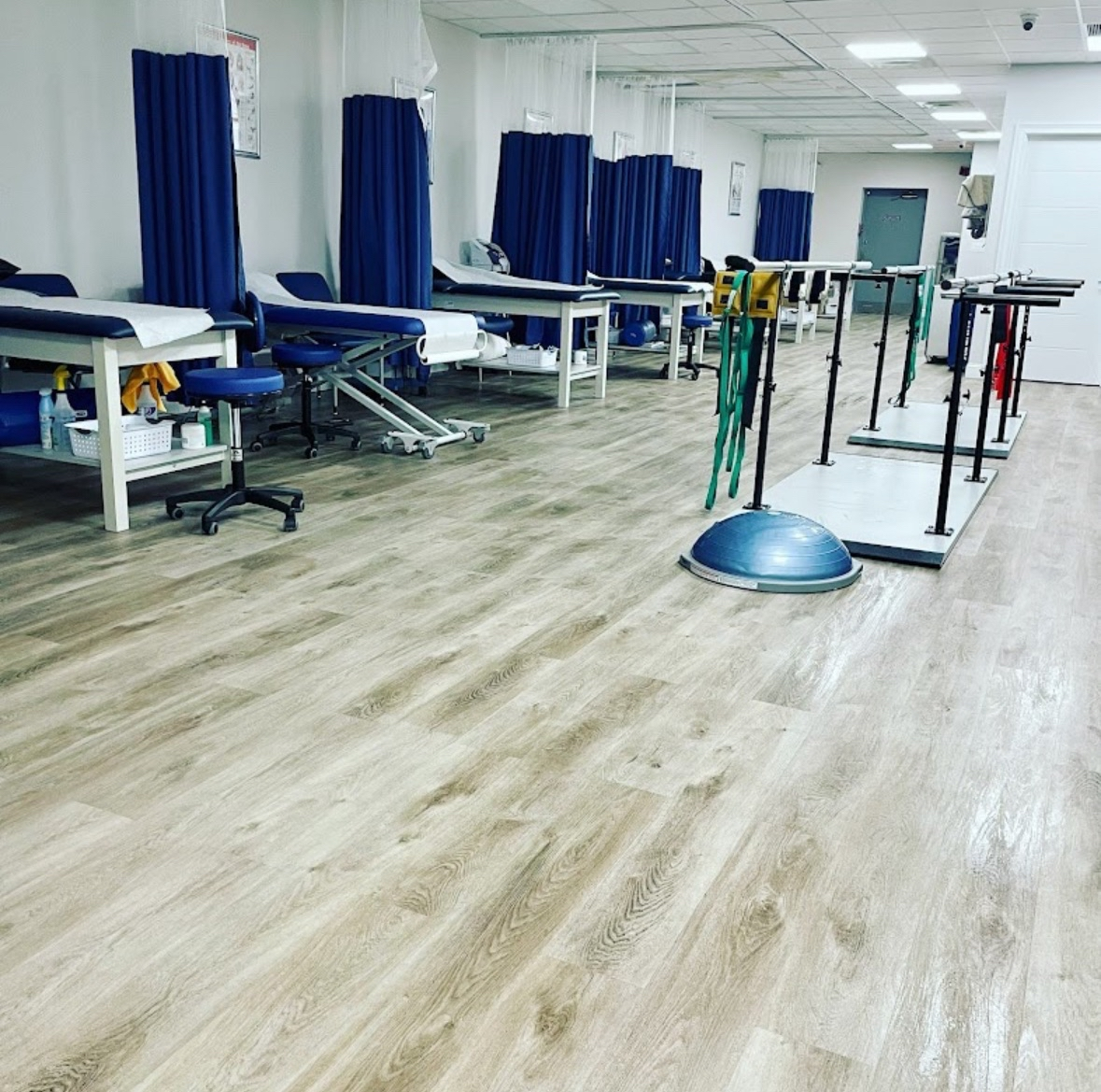 Clean physical therapy room with polished wood-look floors and treatment tables